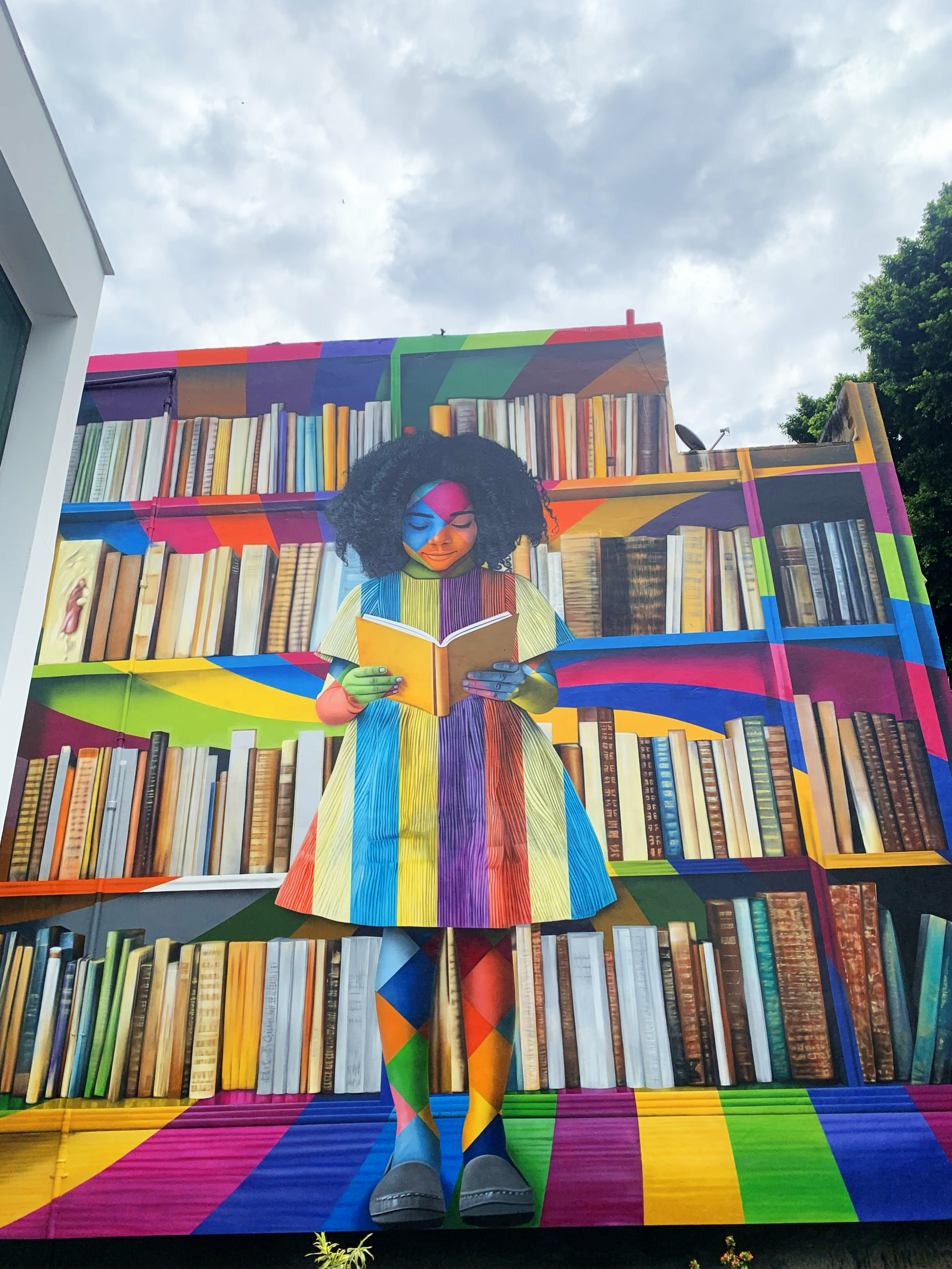 Mural urbano colorido com rostos humanos em composição geométrica, pintado em parede externa da cidade, com atmosfera vibrante de celebração da diversidade cultural